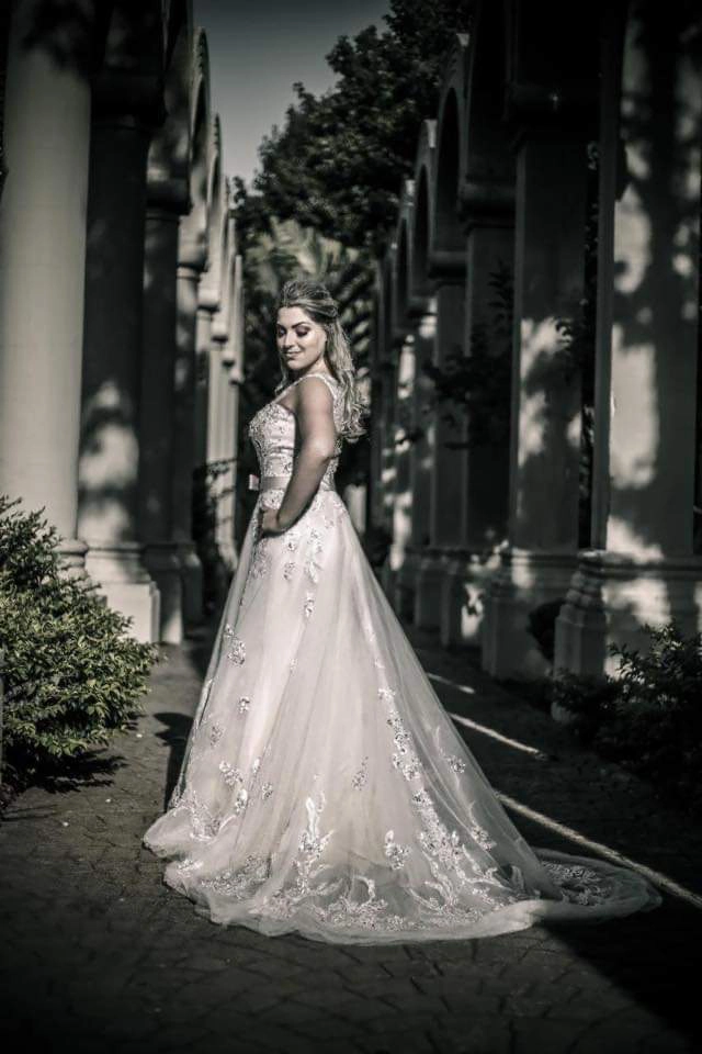 Noiva de vestido rendado caminhando entre colunas em um jardim